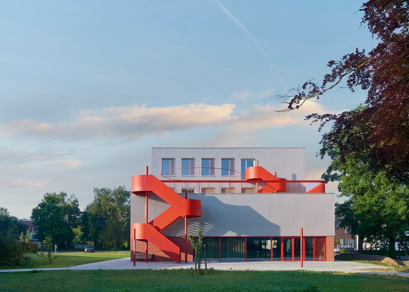View of the building with red exterior staircase and corrugated metal cladding across a green lawn at dusk