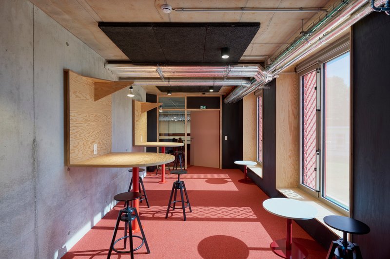 Interior workspace with plywood casework, concrete ceiling, terracotta flooring, and exposed conduit near a window