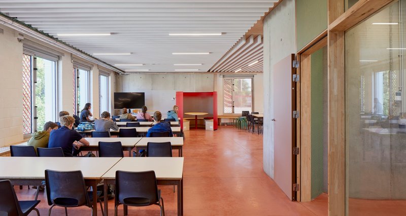 Meeting room with occupants at tables under timber and white acoustic ceiling panels with daylight from left
