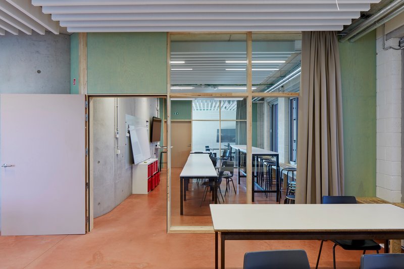 Glass-enclosed meeting room with timber frame visible through adjacent work space with beige flooring and curtain dividers