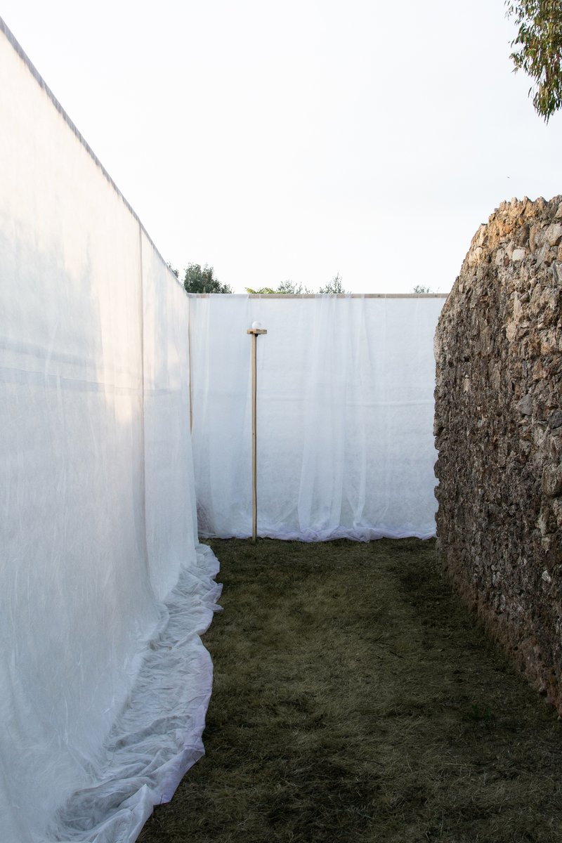 Narrow passage between white fabric screen and rough stone wall with timber prop