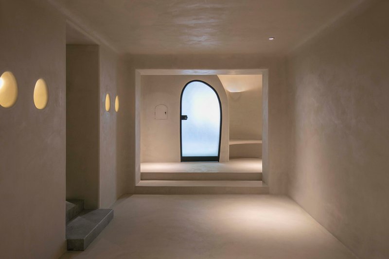 Plastered interior room with circular wall sconces and arched doorway framing a view to the sky