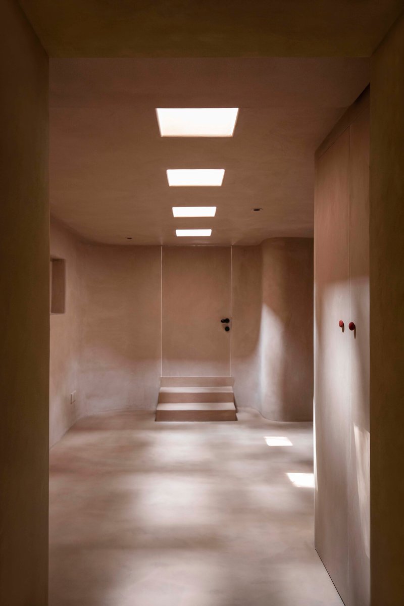 Corridor with four recessed ceiling lights illuminating plastered walls and a stepped threshold ahead
