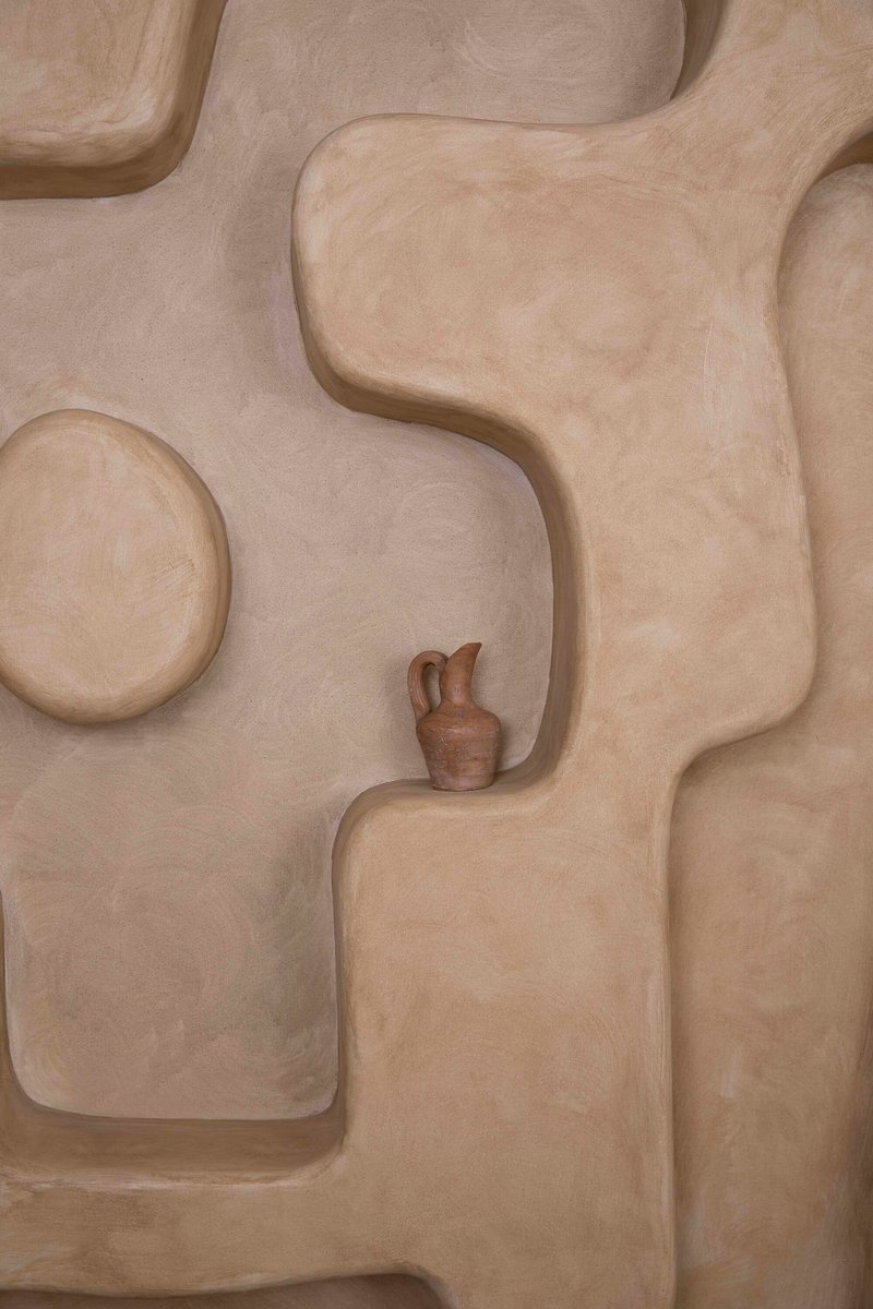 Close-up of plastered wall shelving with organic curved niches holding a ceramic vessel