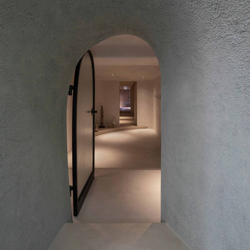 Arched doorway with black metal door frame opening onto a plastered hallway with embedded lighting