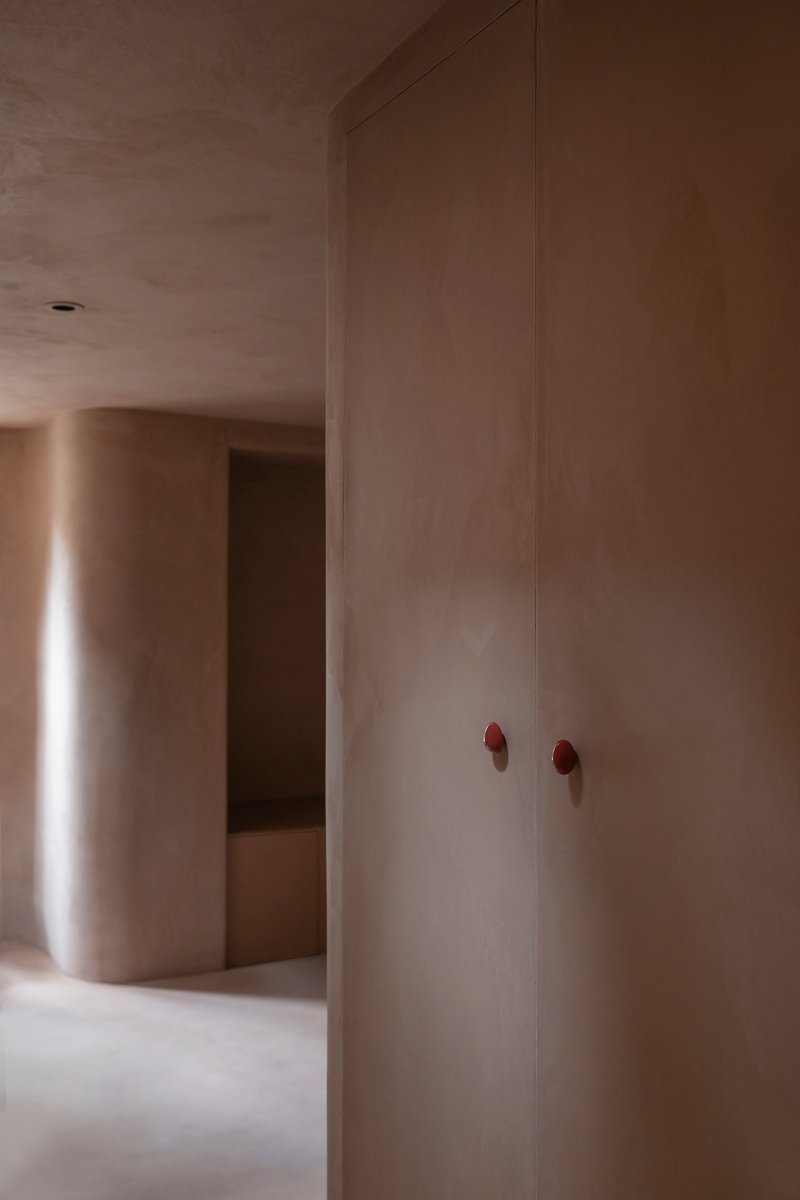 Plastered wall panels with bronze hardware at a corner threshold between two softly lit rooms