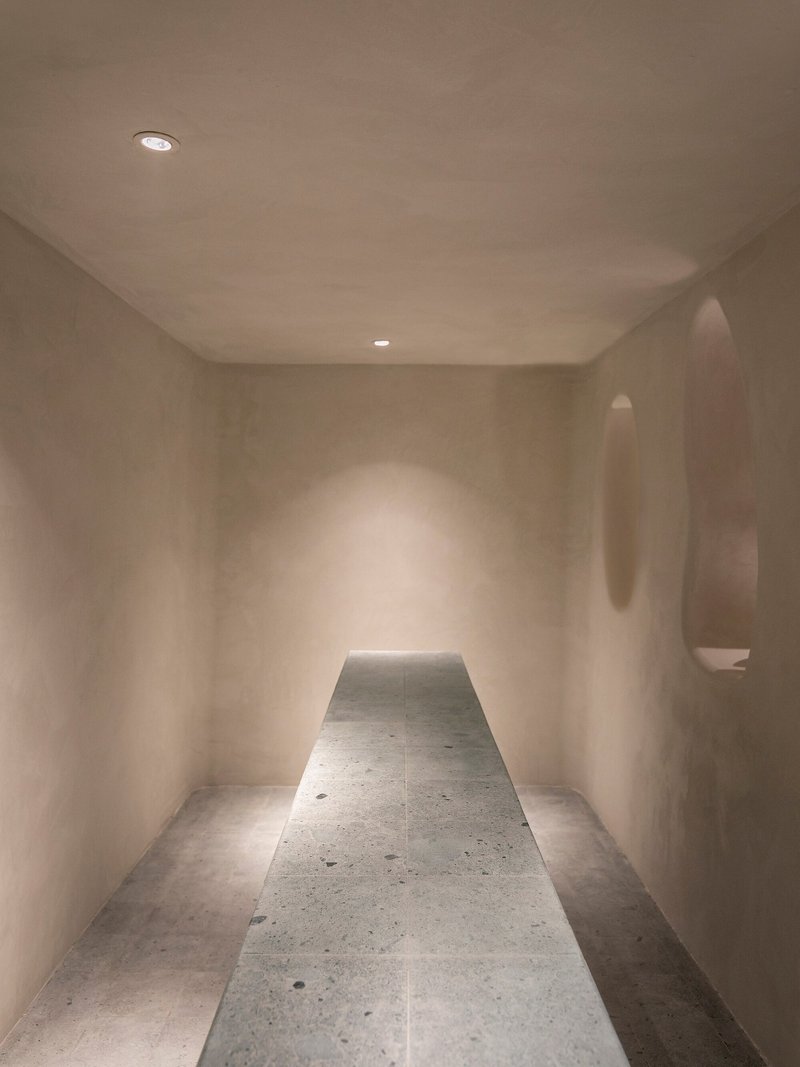 Narrow room with terrazzo floor panel and oval wall niches illuminated by recessed ceiling lights