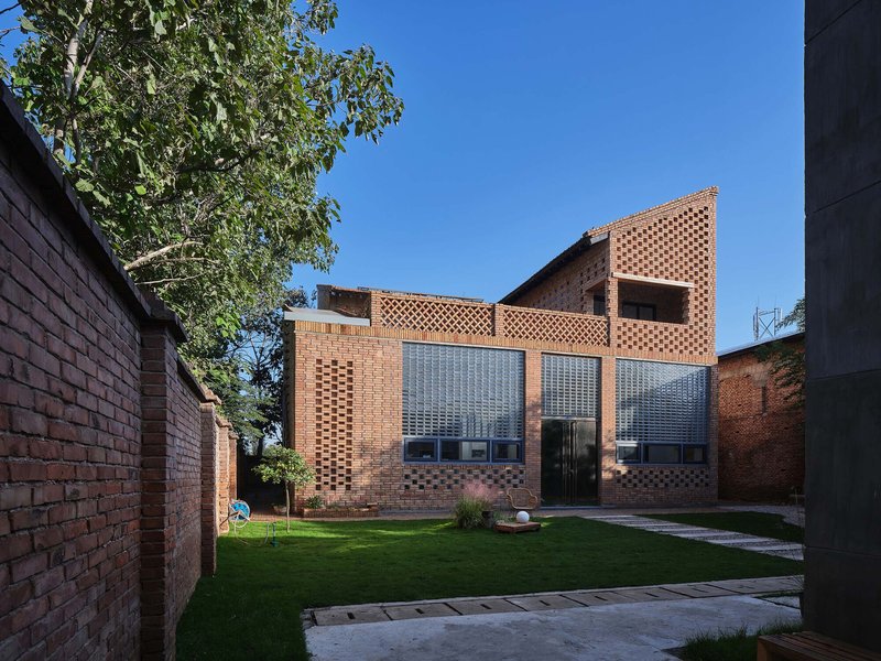 Rear courtyard view showing patterned brick facade with glass block openings and lawn under blue sky