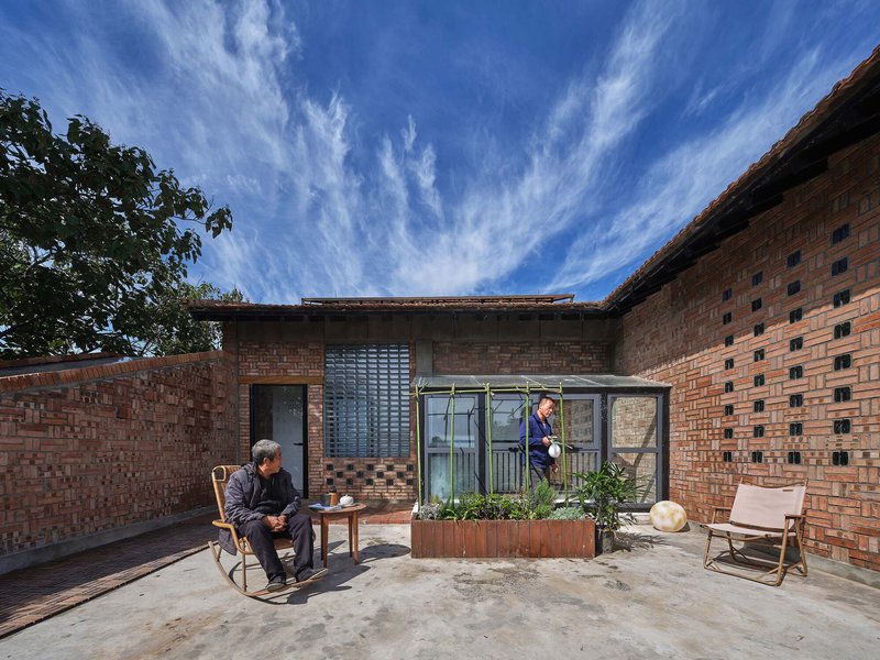 Courtyard terrace with planted bed in metal planter and two seated figures beneath open sky
