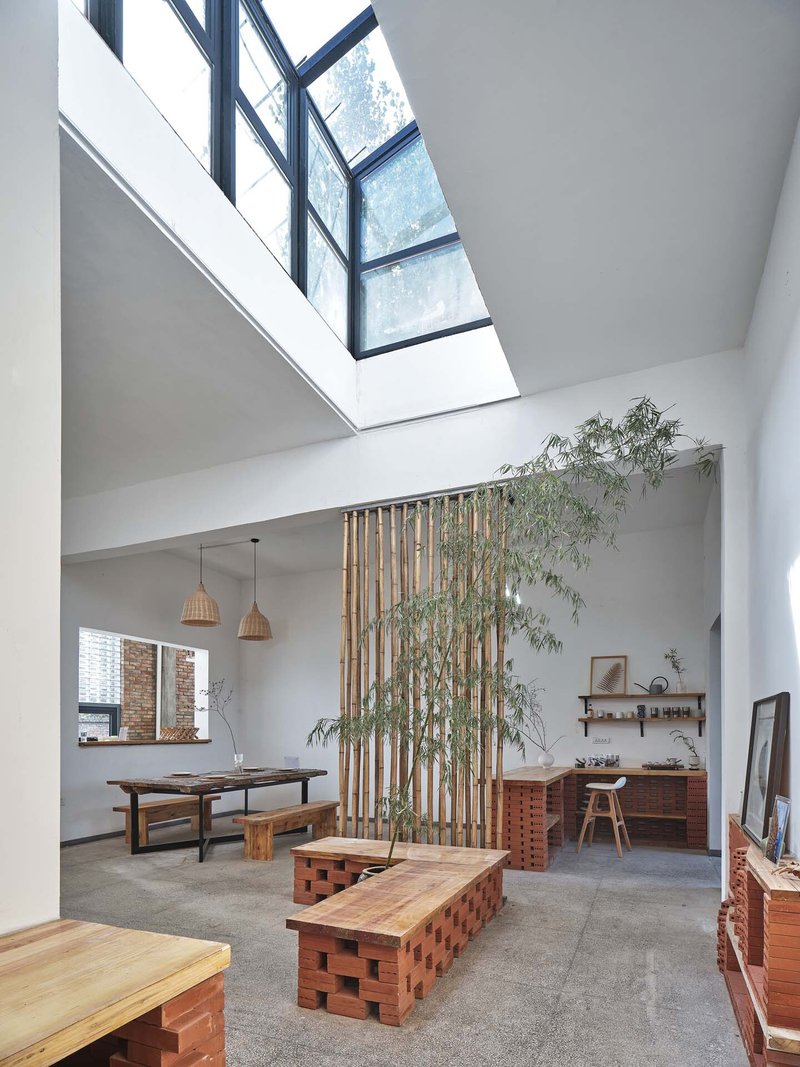 Double-height space with vertical bamboo screen, sloped skylight, and perforated brick furniture on concrete floor