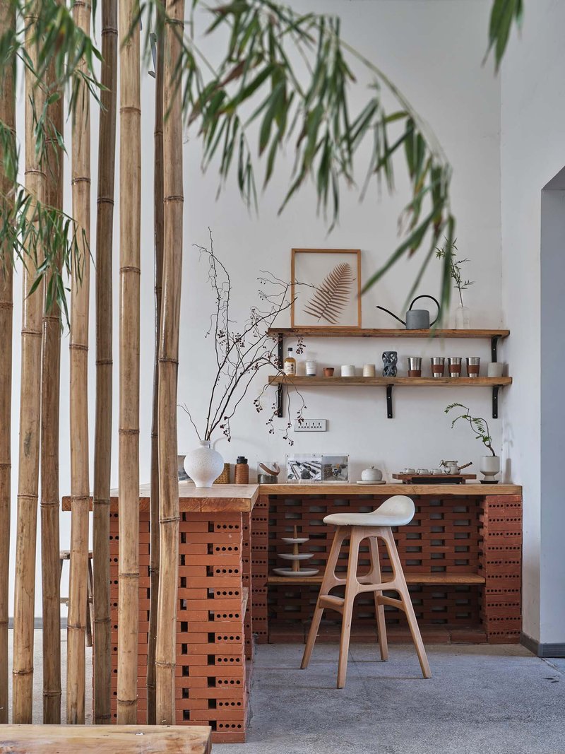 Kitchen counter with perforated red brick base and timber shelving behind bamboo screen