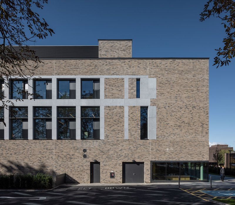 Street facade with pale brick and recessed white concrete frames around tall windows beneath a blue sky
