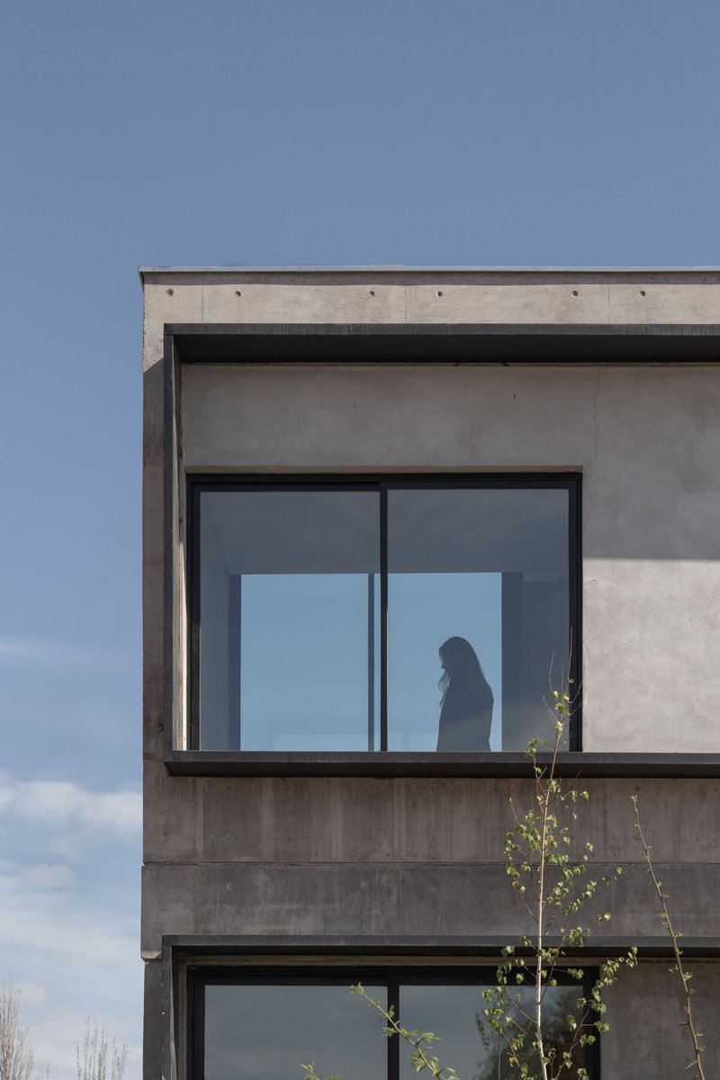Upper level corner detail showing board-formed concrete facade with figure silhouetted behind glazing at dusk