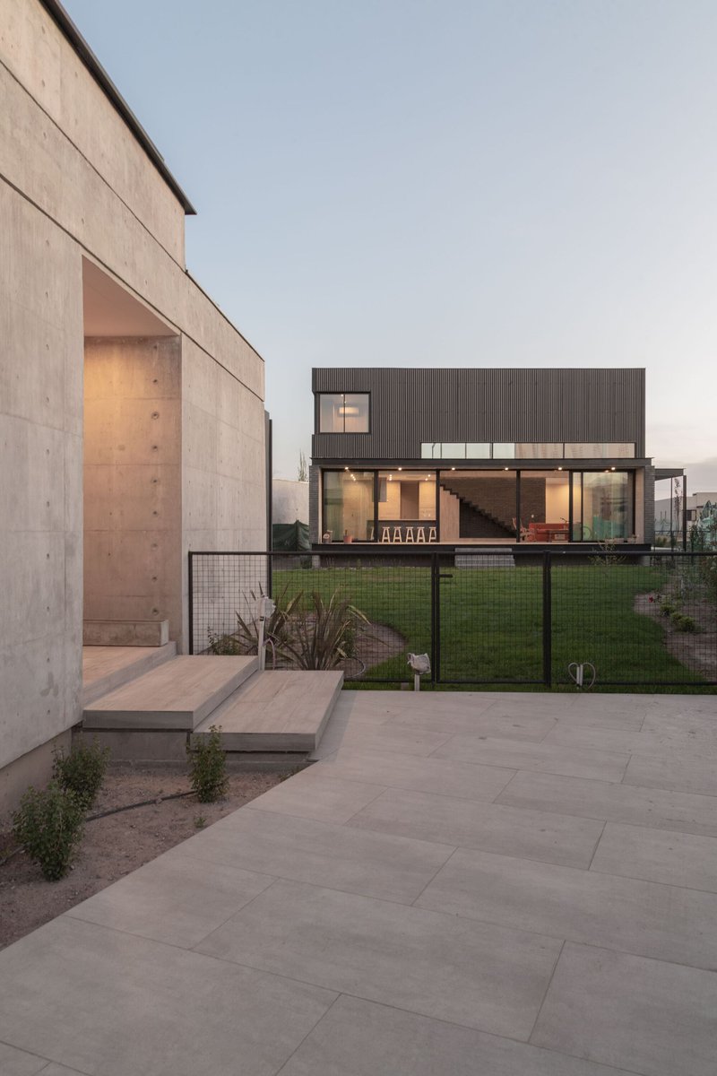 Evening view across the paved terrace showing the glazed living area and concrete wall volumes