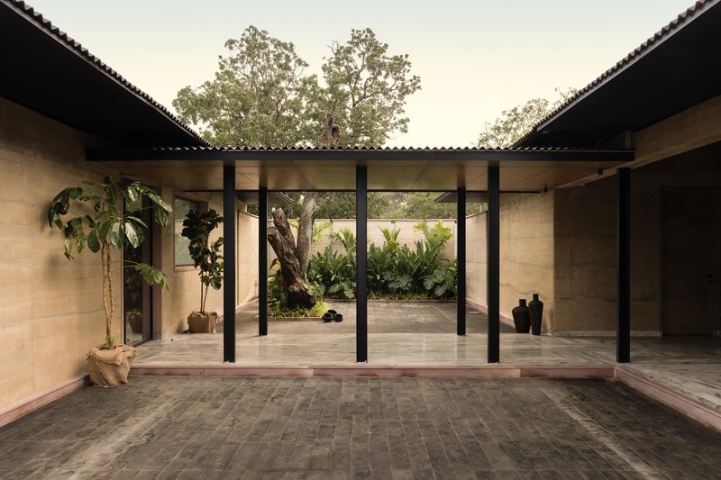 Covered courtyard passage with black steel columns, corrugated roof and planted garden beyond glass walls