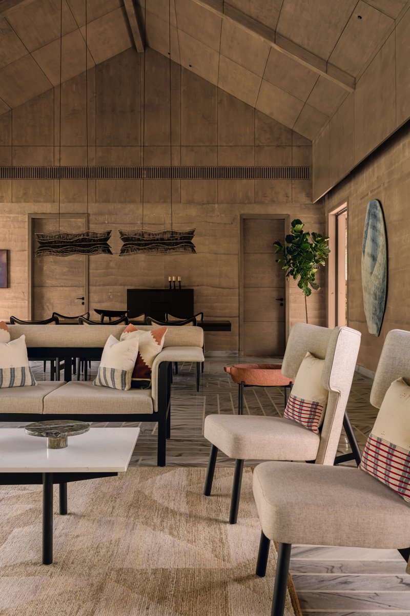 Open-plan living and dining space with vaulted timber ceiling and rammed earth wall panels