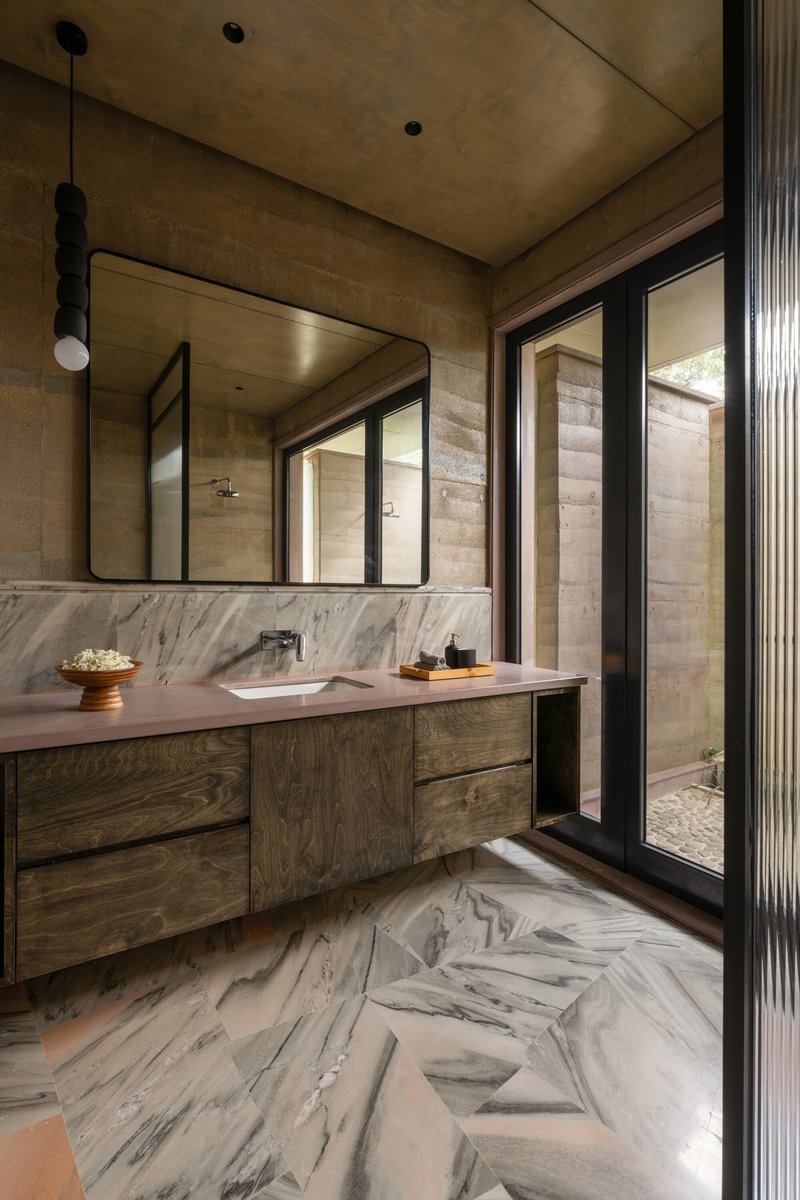 Bathroom with marble flooring and wall cladding, timber vanity, and glass door opening to courtyard