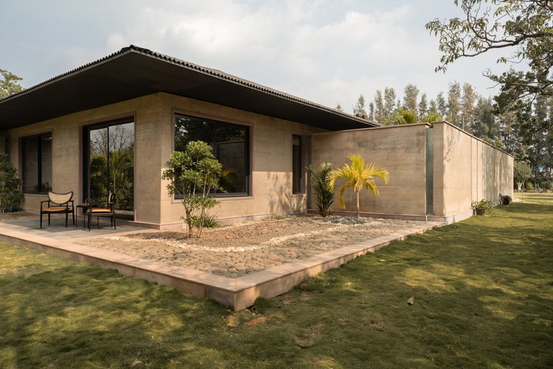 Corner view of the rammed earth pavilion with planted courtyard and deep overhanging roof