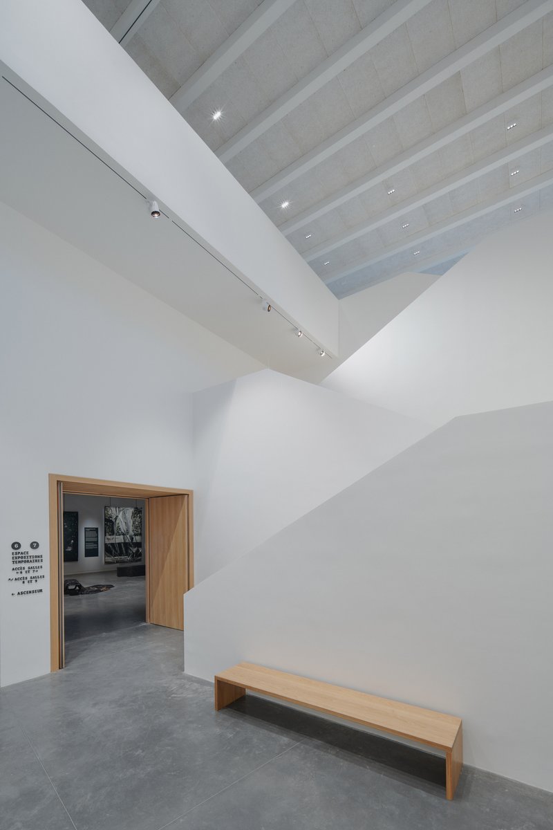 Gallery entrance with timber doorway and bench beneath a ribbed skylight and white walls