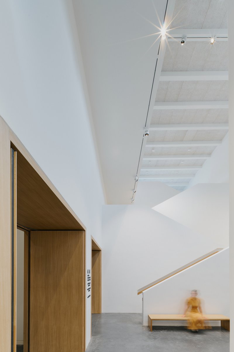 Corridor with timber doorways and a blurred figure passing a bench under pendant lighting
