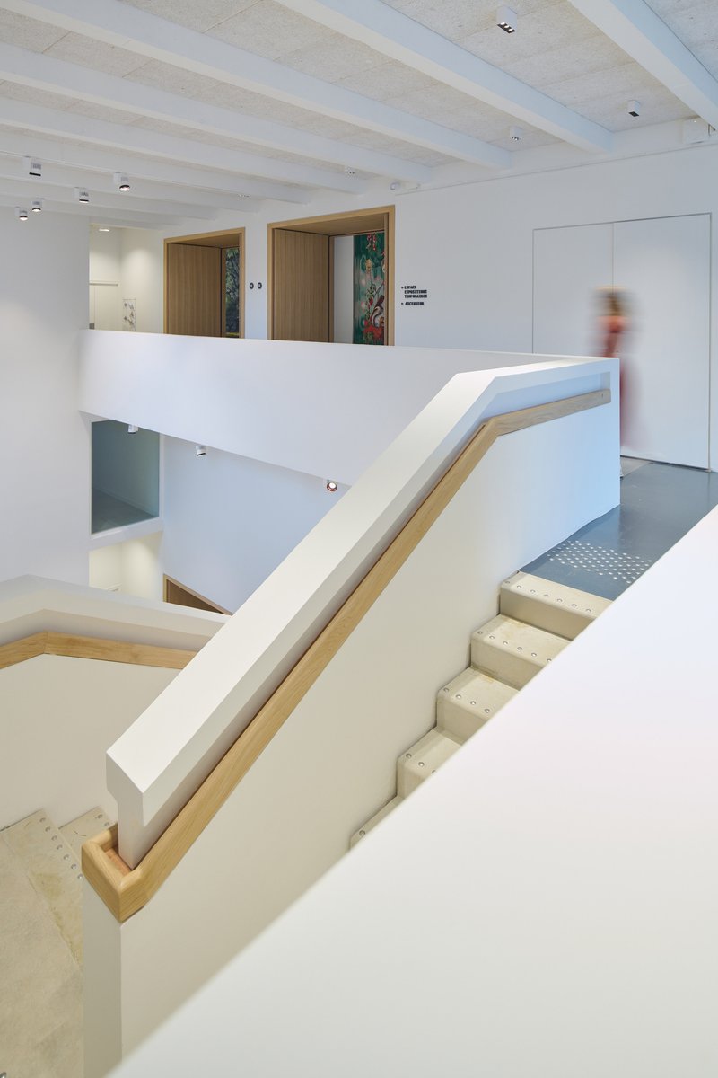 Staircase with white walls and timber handrail connecting multiple levels with a blurred visitor