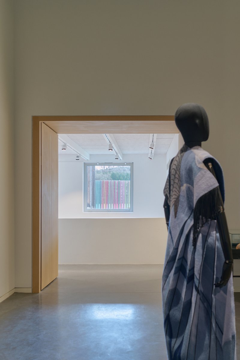 Gallery view through timber doorway with sculpture in foreground and window framing trees beyond