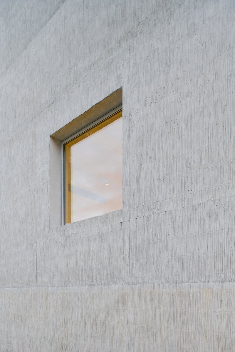 Recessed window with brass frame set into a pale concrete facade with vertical formwork texture