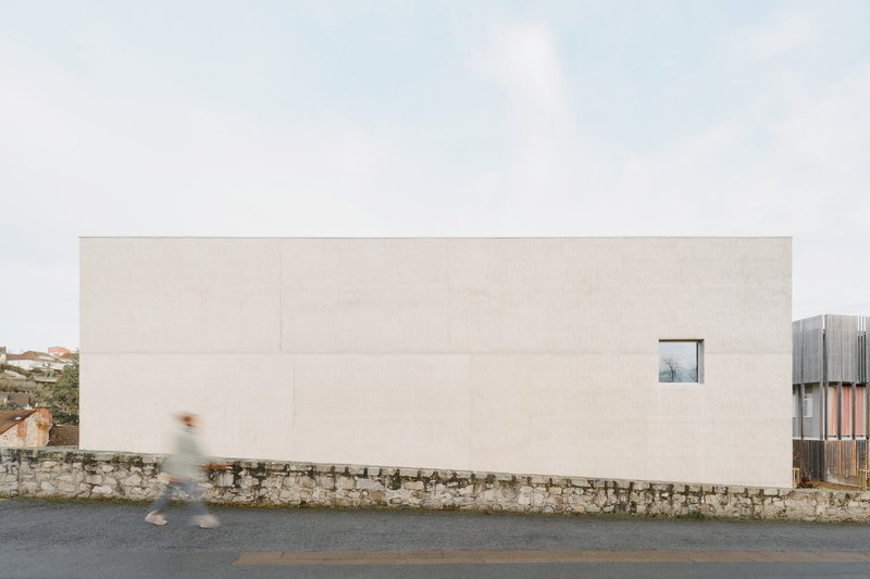 Pale concrete facade with single window above a stone retaining wall as a figure passes