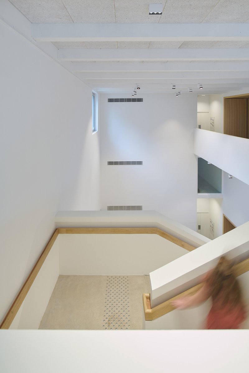 Looking down into a double-height stairwell with white walls and a figure descending the handrail