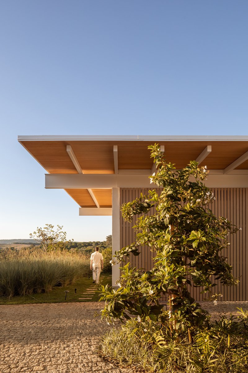 Overhanging timber roof with exposed beams above vertical slat facade and a figure walking at dusk