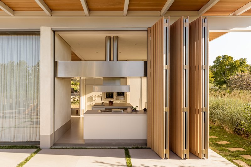 Folding timber screen panels opening the kitchen to a terrace with grass joints at dusk