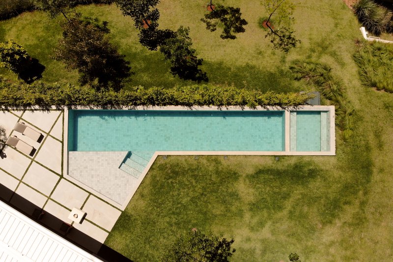 Aerial view of rectangular lap pool with concrete deck surrounded by lawn and scattered trees