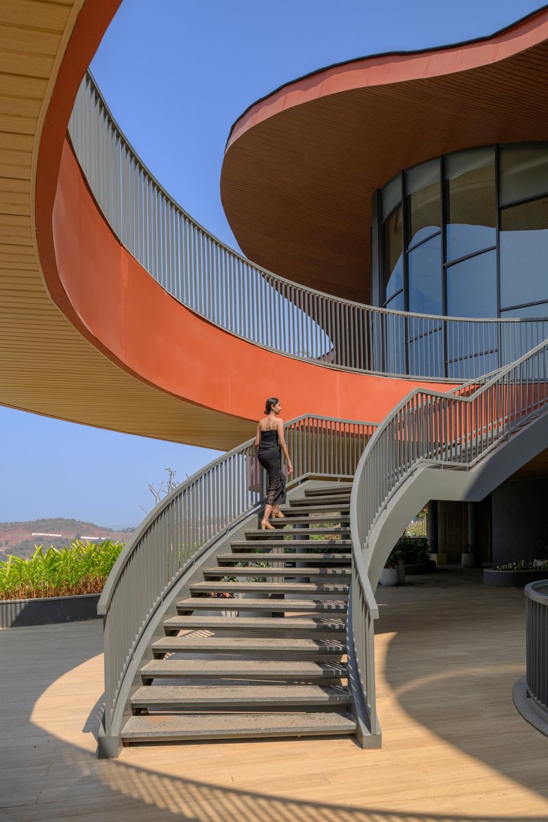 Curved exterior staircase with open risers and a person ascending under blue sky