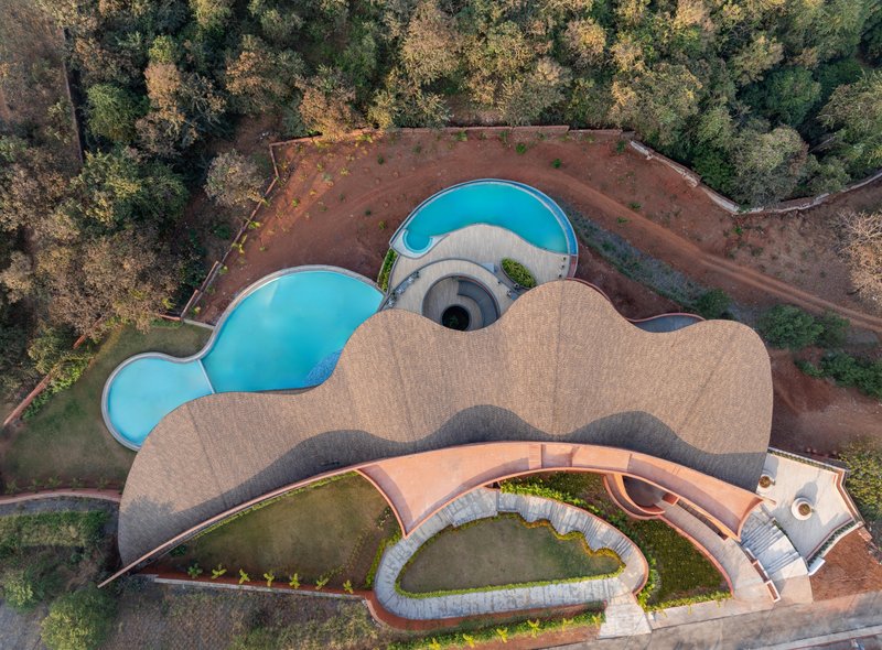 Drone view of the organic roof form with lobed pools and courtyards carved into red earth