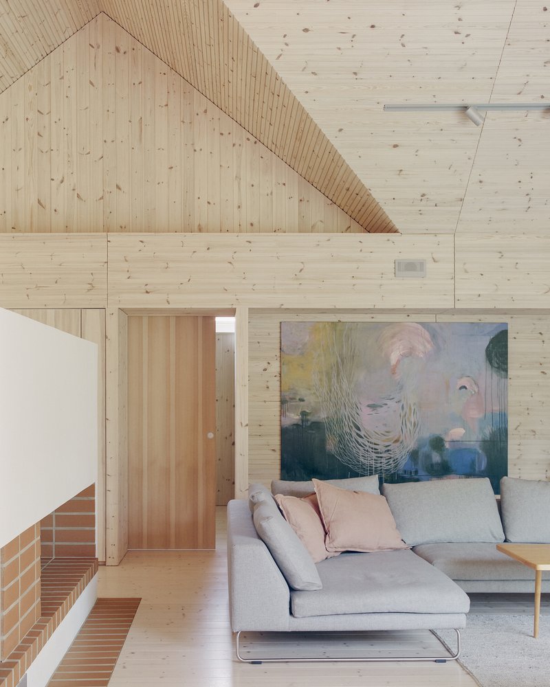 Interior living space with exposed timber plank walls and ceiling above a sofa and brick fireplace surround
