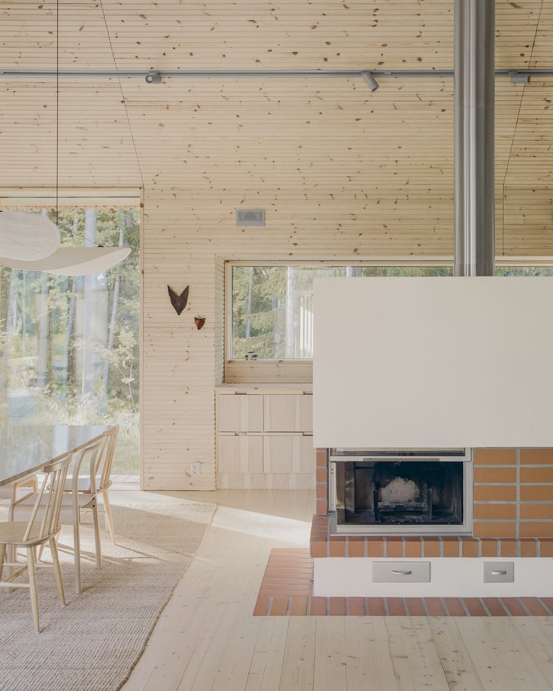 Open dining area with timber walls and tiled fireplace mass framing views to the forest beyond