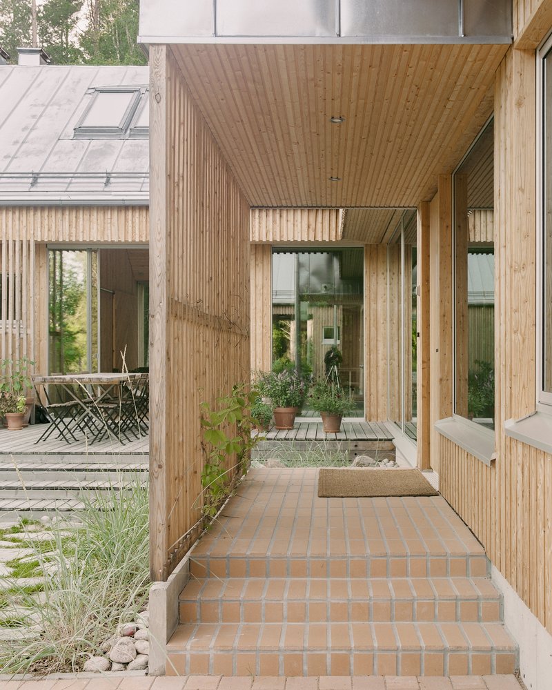 Brick-paved walkway passing timber-clad volumes opening to a planted courtyard with grasses