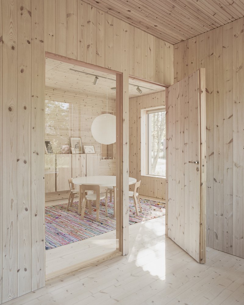 Timber-paneled hallway with open doorway framing dining room with pendant light and colorful rug
