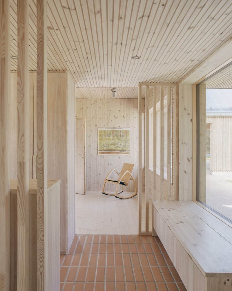 Entry threshold with terracotta tile floor leading to light timber interior with rocking chair and timber slat ceiling