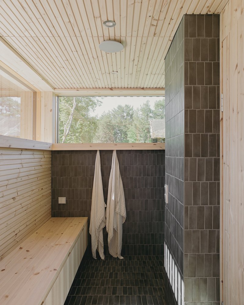 Timber sauna interior with dark tile wall and floor, folded benches, and window overlooking trees