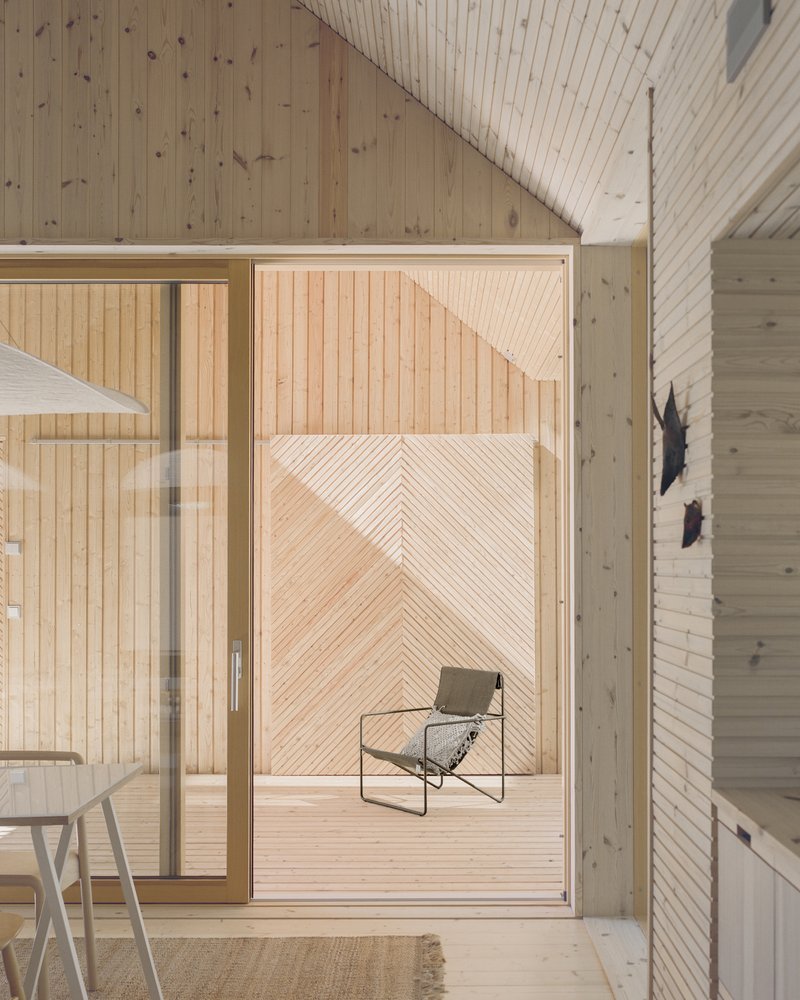 View through sliding glass door to timber deck with lounge chair framed by diagonal wood paneling