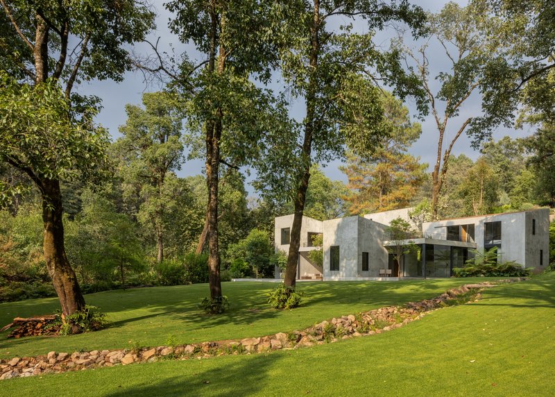 Rear elevation of concrete volumes on sloped lawn with curved stone border and mature trees