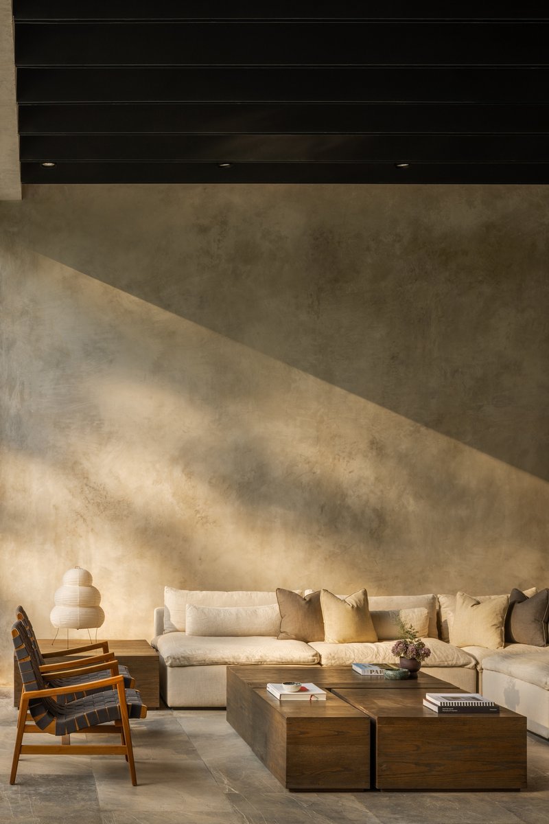Concrete wall with dappled shadows cast across its surface above a seating arrangement with timber tables