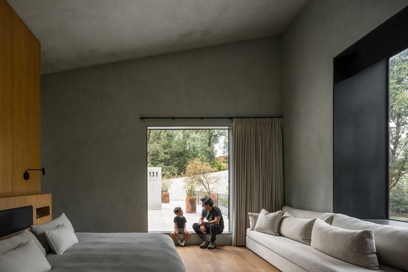 Bedroom with polished concrete walls and two figures seated by the glazed opening to the courtyard
