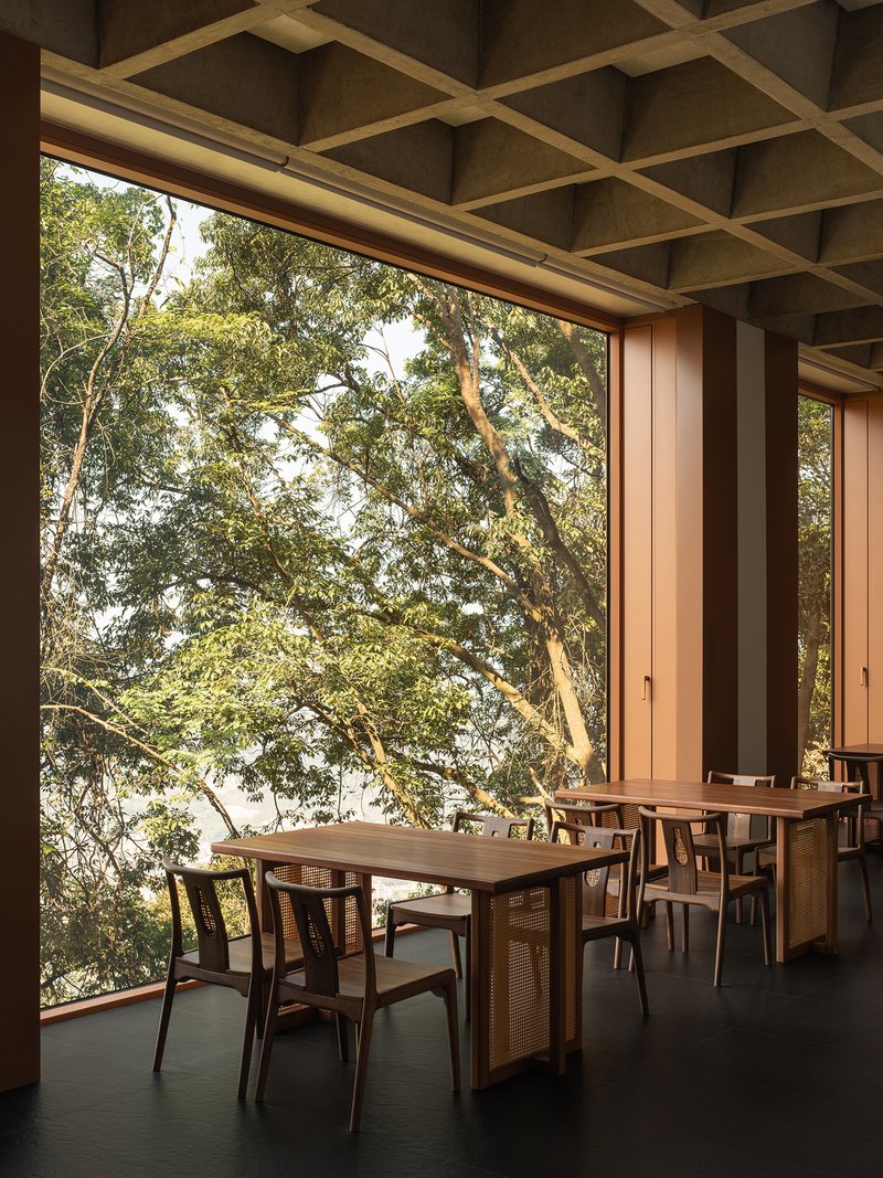 Dining terrace with coffered ceiling and floor-to-ceiling glazing opening onto a tree canopy