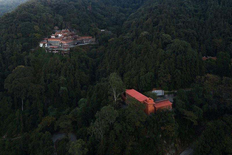 Aerial view of the red-roofed volumes nestled in dense forest at dusk