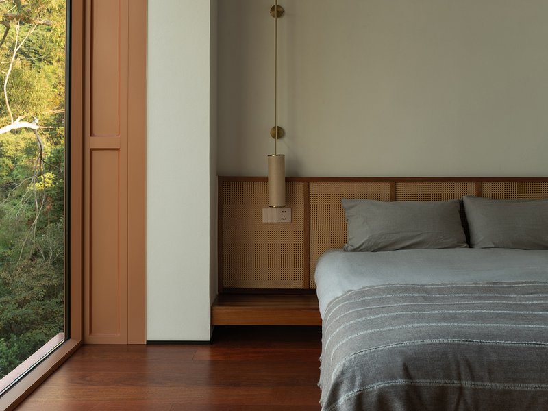 Bedroom with cane-paneled headboard wall and pendant light beside a full-height glazed door