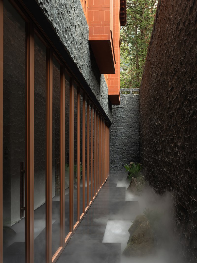 Narrow walkway with timber slat facade and stacked stone walls framed by tree trunks