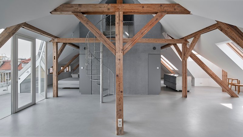 Attic interior with exposed timber trusses, wire mesh spiral staircase, and polished concrete floor under skylights