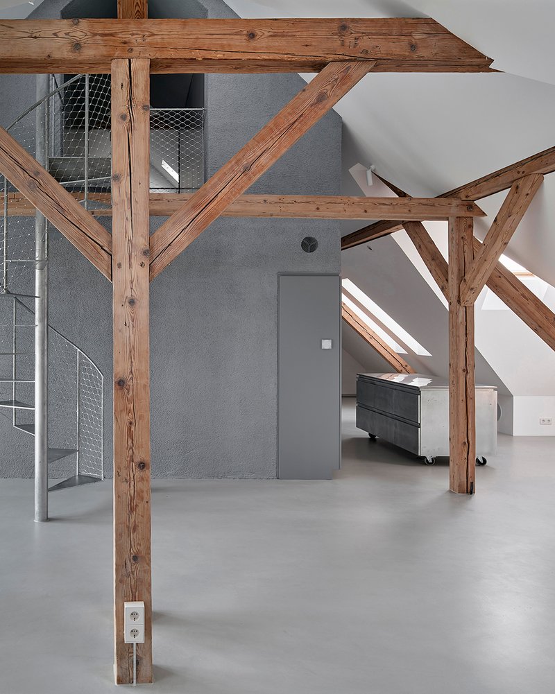 Grey freestanding volume with flush door beneath timber roof structure and adjacent wire mesh staircase